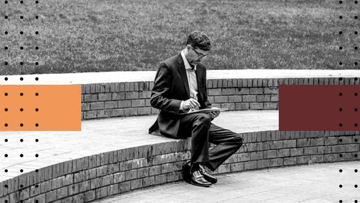 Businessman sitting in outdoors urban park using tablet. City buildings visible in background.