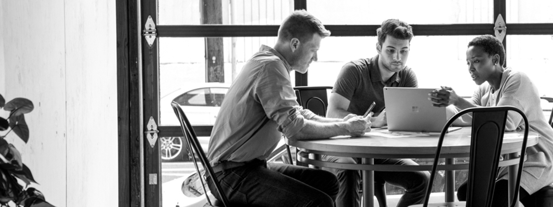 Three people sitting around a table looking at a laptop.