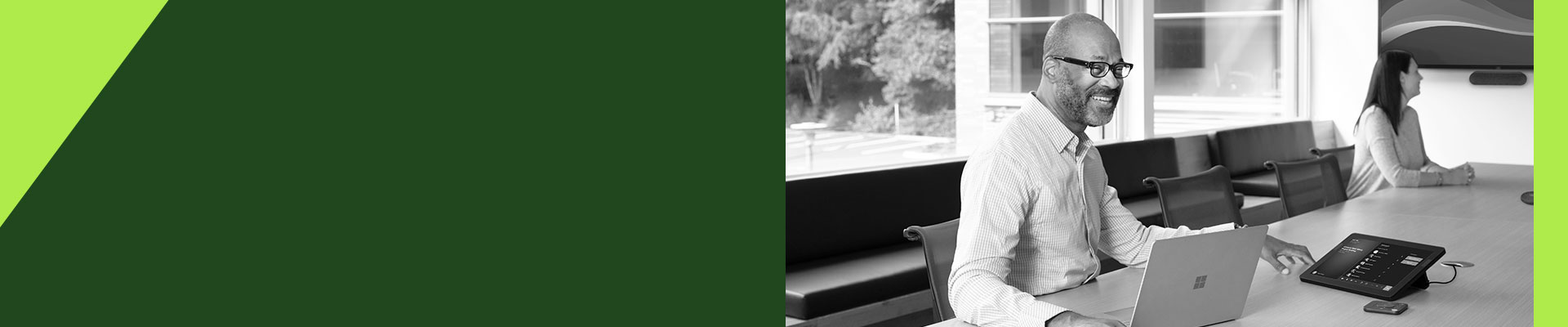 Man with a laptop working at a conference table with another person nearby