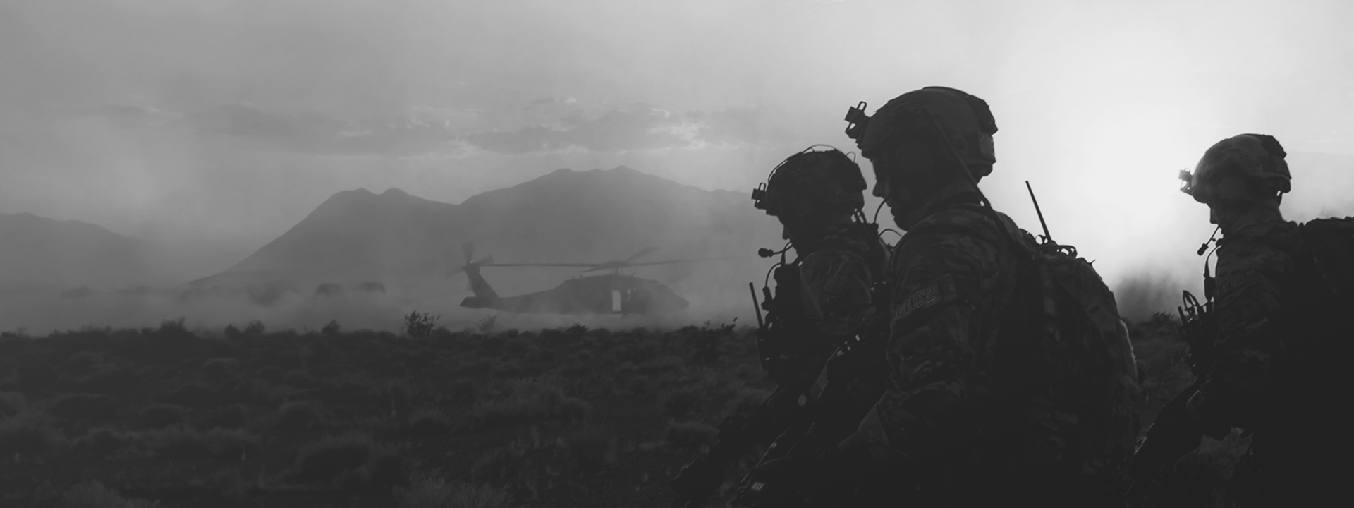 Three soldiers walking in the desert with a helicopter in the background