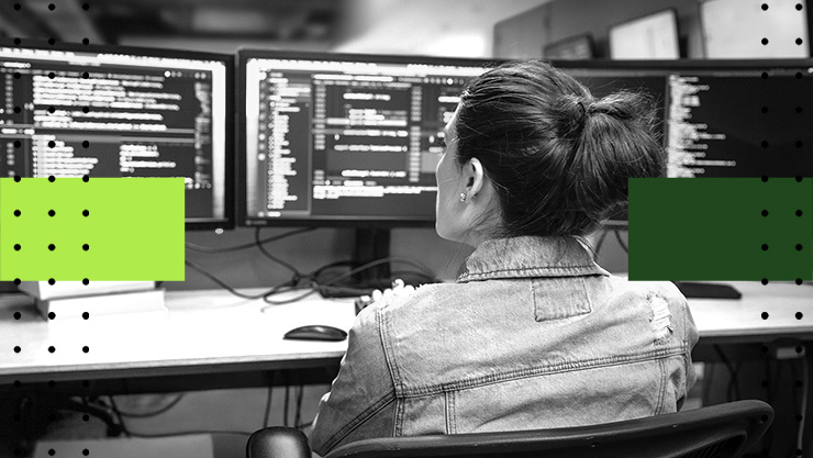 A woman sitting at a desk with three computer monitors displaying code