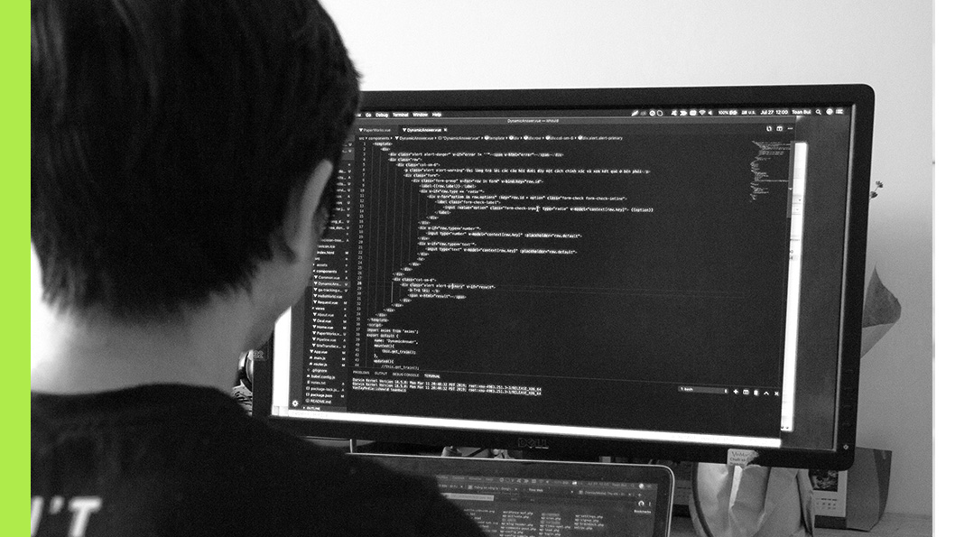 An individual viewed from behind, staring at a coding-filled screen.