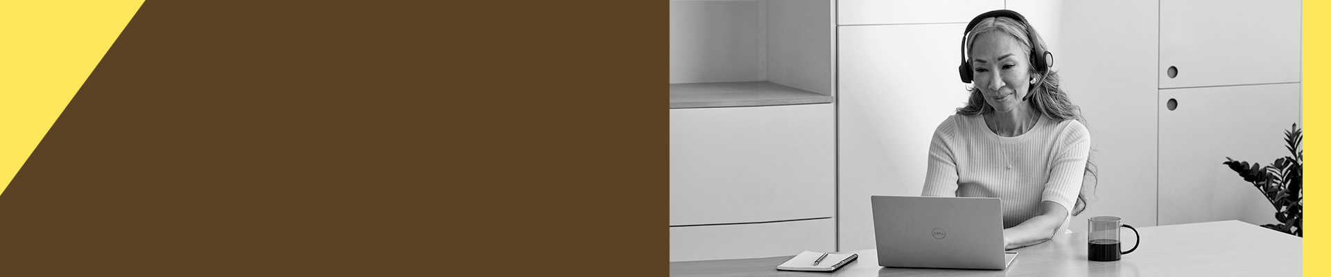 Person wearing a headset using a laptop at a desk with a coffee mug.