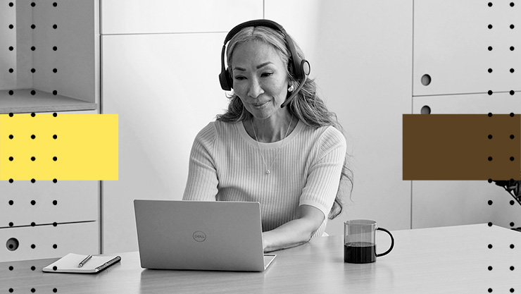 Person wearing a headset using a laptop at a desk with a coffee mug.