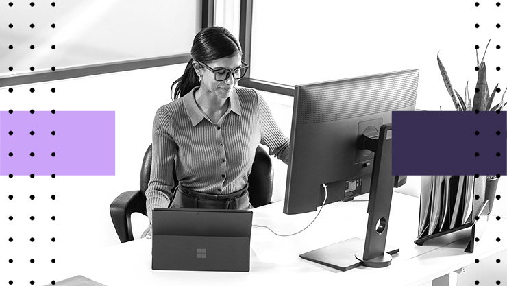 Person working at a desk with a laptop and external monitor in a bright office
