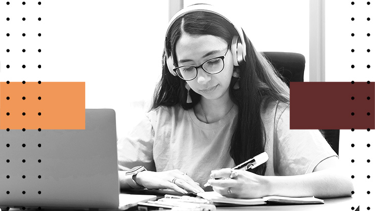 Person wearing headphones writes in a notebook beside a laptop with graphic shapes in the background.