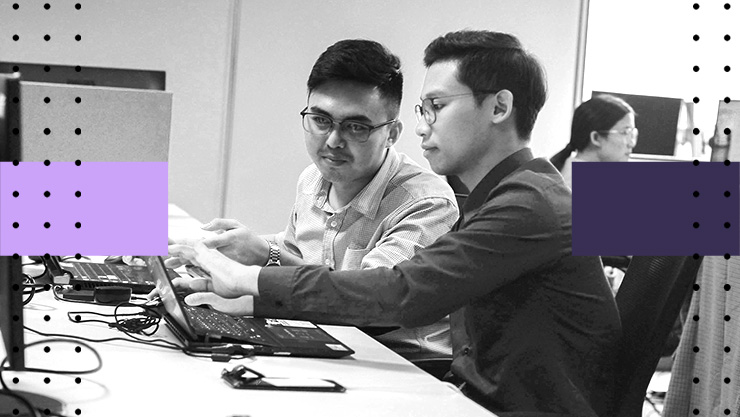 Two people sit side by side, collaborating on a laptop in an office workspace with graphic overlays.