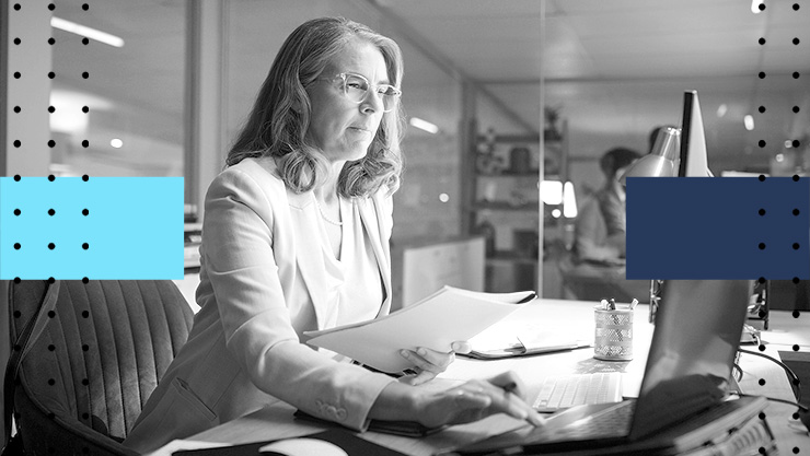 Person reviewing documents while working on a laptop in a modern office.