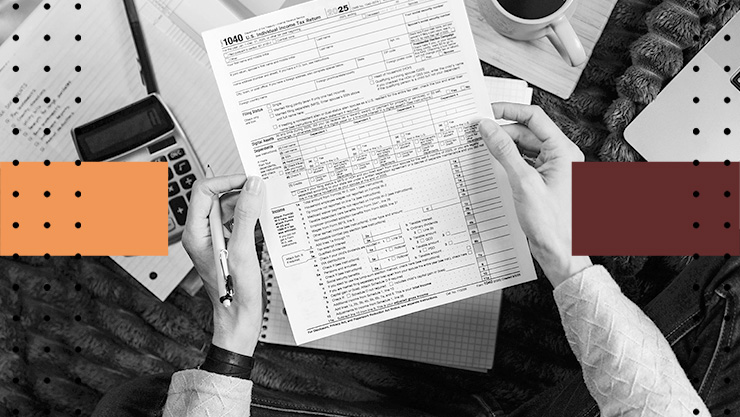 Hands holding a 1040 tax form over a desk with a calculator, notebook, coffee cup, and laptop in a black‑and‑white workspace.