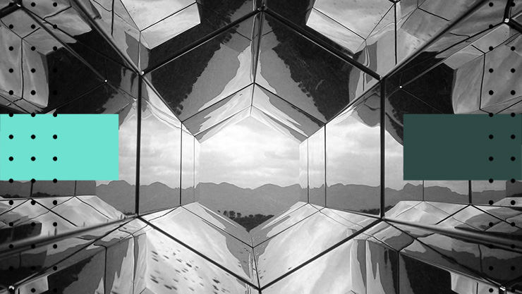 Black-and-white view through a mirrored geometric structure, creating a symmetrical hexagonal frame around a distant mountain landscape.